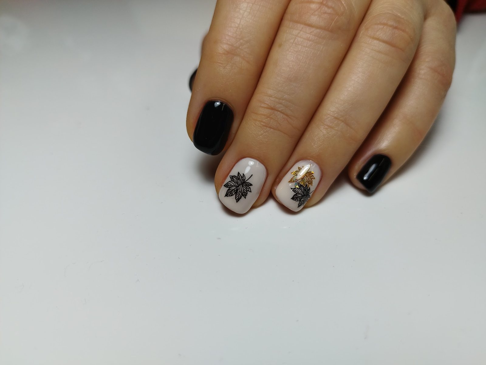 Korte nagels in zwart en crème met een bladstempel en goud